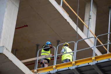 İki erkek işçi inşaat alanında iskelede dikilirken, açık gökyüzü altındaki görevlerine odaklanarak tartışmaya başladılar..