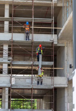 İnşaat işçileri gündüz saatlerinde bir inşaat alanında inşaat iskelesi kuruyorlar.