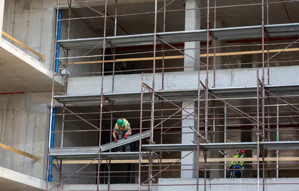 İnşaat işçileri gündüz saatlerinde bir inşaat alanında inşaat iskelesi kuruyorlar.