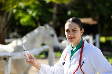 Kadın veteriner portresi, elinde şırıngayla çiftlikte at aşılamaya hazır.