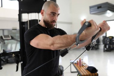 Spor salonundan terleyen kendine güvenen erkek portresi, kol egzersizi için ekipman kullanıyor.