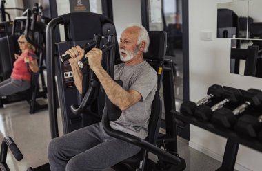 Yaşlı spor partnerleri eğitim için sinek makineleri kullanıyor, ekipmanları güvenli ve kolay bir şekilde kullanan yaşlı adama odaklanıyor.