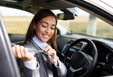 Kadın arabada otururken emniyet kemerini bağlarken gülümsüyor. İçerisi modern ve gündüz gözüyle aydınlık.