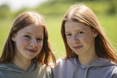 Güneşli bir bahar gününde çilli ikiz kız kardeşlerin portresi. Kameraya bakarken yüzlerinde gülümseme var.