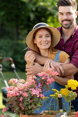 Güneşli bahçede renkli çiçeklerle çevrili neşeli çift kucaklaşır. Bahçe işleriyle meşguller, takım çalışmalarını ve neşelerini sergiliyorlar..