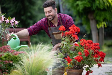 İnsanlar saksılarda çiçekleri dikkatlice sularken aynı zamanda çeşitli bitkilerle dolu huzurlu bir bahçede huzurlu bir öğleden sonra geçiriyorlar.
