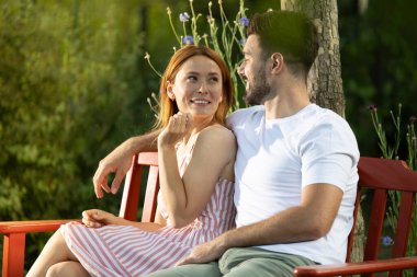 Parkta güzel bir çiftin üzerine güneş doğuyor. Kırmızı bankta oturup mutlu bir şekilde birbirlerinin gözlerinin içine bakıyorlar. Adamın kız arkadaşının kollarına sarılıyorlar.