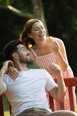 Güzel genç bir kadın, yakışıklı erkek arkadaşına parkta arkadan sarılmaya gider. Adam bankta otururken mutlu bir şekilde omzunun üzerinden ona bakar.