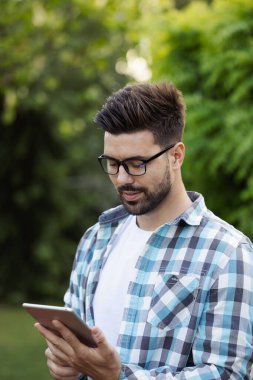 Yakışıklı bir adam, dışarıdayken dijital tabletine dikkatle bakıyor.