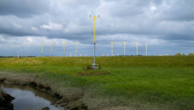 A row of approach lighting system (ALS) with sequenced flashing lights, commonly used at airports to guide aircraft during the landing phase. The lights are mounted on tall, slender yellow poles, arranged in a straight line receding into the distance clipart