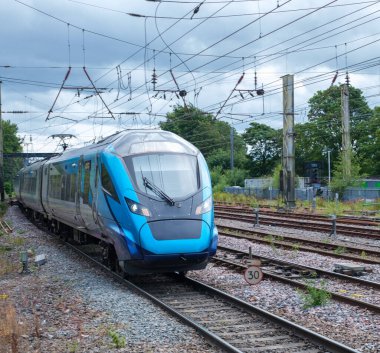 Pürüzsüz mavi bir tren bulutlu gökyüzünün altında hızla ilerliyor, çağdaş ulaşım ve dinamik seyahat sergiliyor. Modern altyapı ve kentsel hareketlilik temaları için mükemmel