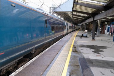 Durgun bir trenle bir tren istasyonundaki boş platform, yolculuğun sessiz anlarını yansıtıyor.