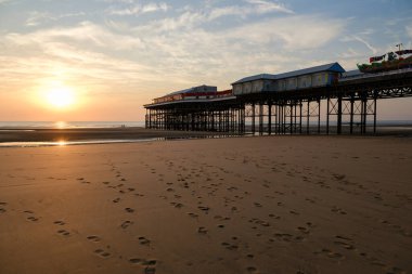 Huzurlu günbatımı manzarası, okyanus üzerinde canlı bir iskeleye doğru giden ayak izleri..