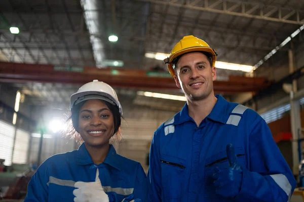 Diversity portrait of Two industrial worker male and Black female looking at camera wearing hard hat helmet in factory.