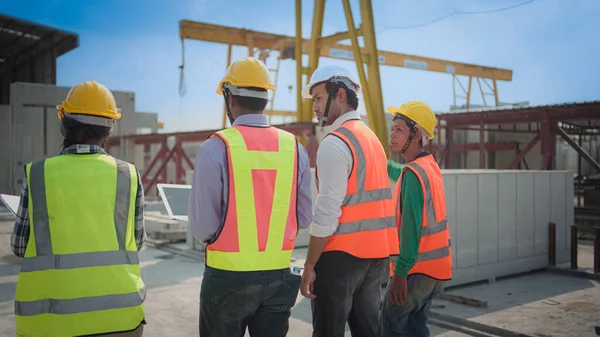Back view of Asian civil engineer or Architect, inspector with contractor, foreman or worker wear safety helmet. Colleagues discussing, meeting about construction building project on site.