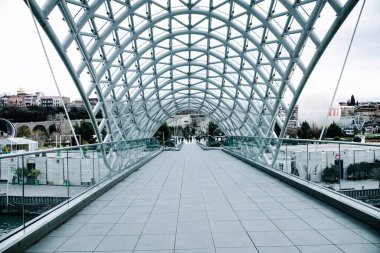 TBILISI, GEORGIA - 08 Ocak 2023: Barış Köprüsü boyunca yayılan insanlar. Modern mimari ve Tiflis Gürcistan 'ın ünlü simgesi..