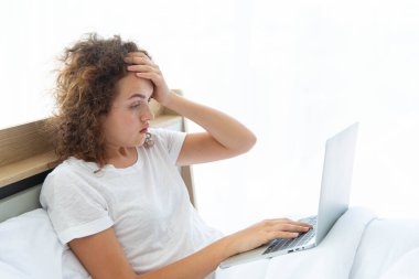 Genç ve güzel iş kadını, sabah uyandıktan sonra yatakta yatarken dizüstü bilgisayarla çalışırken baş ağrısı çekiyor..