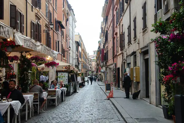 Roma, İtalya, 17 Nisan 2024: Restoranlar ve çiçeklerle süslenmiş balkonlarla dolu hareketli bir Roma caddesi, İtalya 'nın başkentinin canlı günlük yaşam ve kültürünü yakalıyor.
