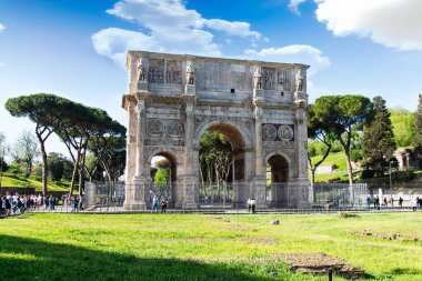 Roma, İtalya-17 Nisan 2024: Roma 'daki Konstantin Kemeri, sembolik bir zafer kemeri, parlak mavi gökyüzüne karşı görkemli bir şekilde duruyor. Yeşillik ve ziyaretçilerle çevrili bu tarihi anıt Konstantin 'in zaferinin anısına yapılmıştır.