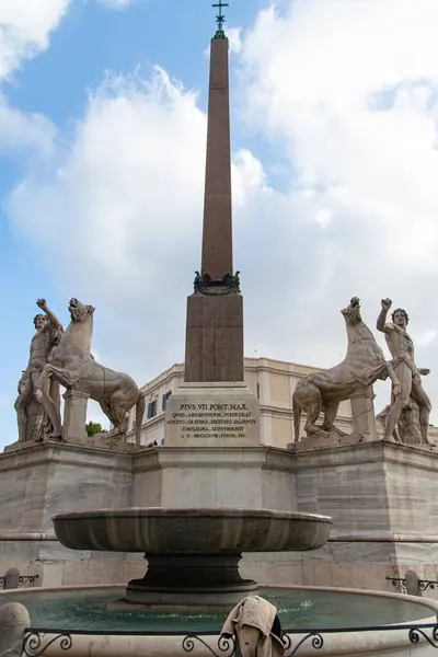 Roma, İtalya-17 Nisan 2024: Roma 'daki Piazza del Quirinale' deki Obelisk heybetli heykellerle çevrili bulutlu bir gökyüzüne karşı dimdik ayakta duruyor. Önde gelen bir meydanda yer alan bu tarihi anıt, kentin zengin mimari mirasına ekleniyor ve