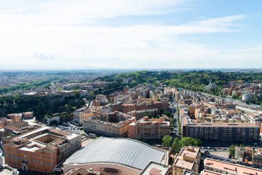 Vatikan, İtalya-18 Nisan 2024: Açık bir gökyüzü altında yerleşim binaları, yeşillikler ve uzak dağların yer aldığı Roma kentsel manzarasına geniş bir hava manzarası.