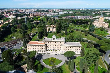 Vatikan, İtalya-18 Nisan 2024: Açık bir gökyüzü altında yerleşim binaları, yeşillikler ve uzak dağların yer aldığı Roma kentsel manzarasına geniş bir hava manzarası.