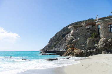 Cinque Terre, İtalya-20 Nisan 2024: Cinque Terre 'de Monterosso sahilinde kayalık sahil şeridinde turkuaz suları ve berrak gökyüzü bulunan etkileyici Neptün heykeli yer almaktadır..