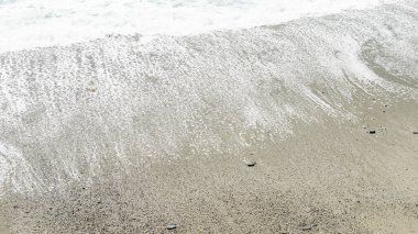 Köpüklü dalgaların yakın çekimi Monterosso, Cinque Terre 'nin kumlu sahillerinde yavaşça süzülüyor, sakin sahil güzelliğini vurguluyor..