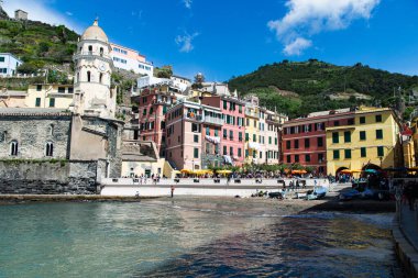 Cinque Terre, İtalya-20 Nisan 2024: Renkli binalar, tarihi bir kilise ve güneşli bir günün keyfini çıkaran turistlerin yer aldığı Vernazza, Cinque Terre 'deki büyüleyici rıhtım.