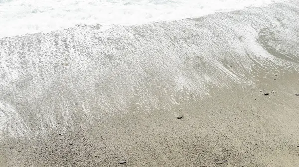 Köpüklü dalgaların yakın çekimi Monterosso, Cinque Terre 'nin kumlu sahillerinde yavaşça süzülüyor, sakin sahil güzelliğini vurguluyor..