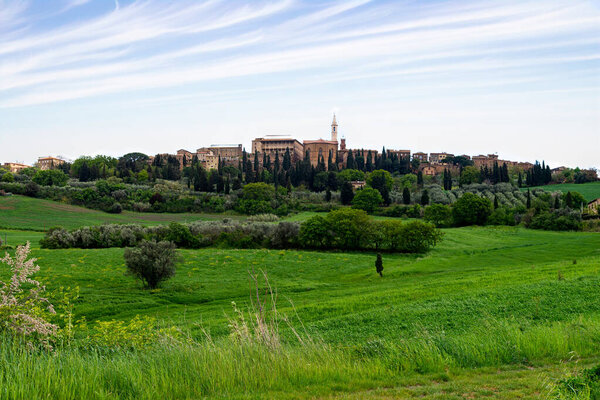 Тоскана, Италия-22 апреля 2024 года: живописный вид на исторический городок на вершине холма, окруженный пышной зеленью и холмами, под частично облачным небом в Тоскане.