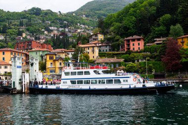 Como Gölü, İtalya-26 Nisan 2024: Como Gölü 'ndeki canlı ve pitoresk Varenna köyüne, yemyeşil tepeler ve renkli binalarla çevrili bir feribot yanaştı.