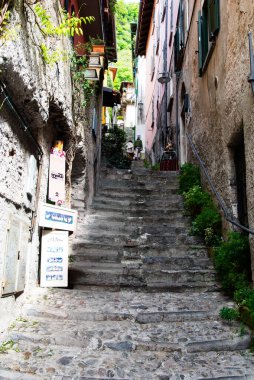 Como Gölü, İtalya-26 Nisan 2024: Tuhaf bir İtalyan köyünde eski binalar arasında dar bir taş merdiven esiyor, yeşillik ve cazibe katan işaretler var..