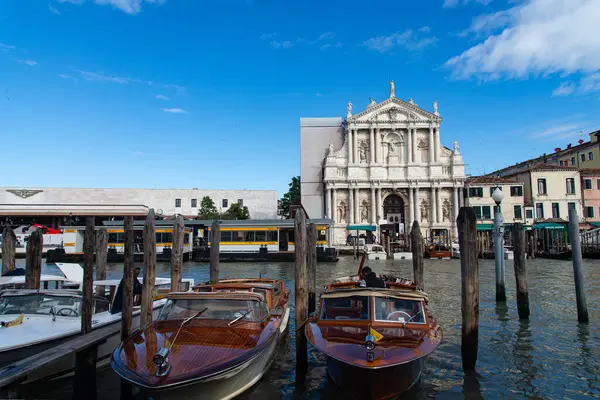 stock image Venice, Italy-April 25, 2024: Water taxis docked in front of Venice's train station with a view of a historic church on a bright day.