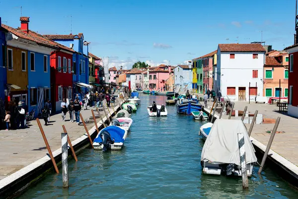 stock image Burano, Italy-April 25, 2024: A lively canal scene in Burano, Italy, featuring colorful houses, boats docked along the water, and pedestrians enjoying the day.