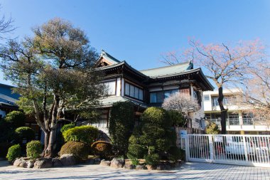 Japonya, 9 Şubat 2025: Manikürlü ağaçlar ve çalılarla çevrili geleneksel Japon ahşap evi.
