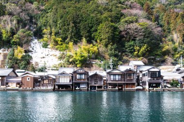 Ine, Japonya, 13 Şubat 2025: Su kenarındaki Ine köyündeki geleneksel kayıkhaneler, ormanlık bir yamaçla destekleniyordu..