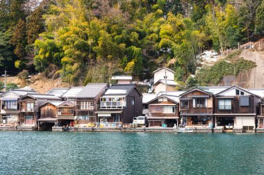 Ine, Japonya, 13 Şubat 2025: Geleneksel kayıkhane köyü Ine, Kyoto 'da günlük hayatın otantik görüntüsü. Yerel halk, yeşil tepelerle çevrili, huzurlu körfez boyunca balıkçı tekneleri ve ev eşyalarıyla büyüleyici rıhtım evlerinde yaşıyor..