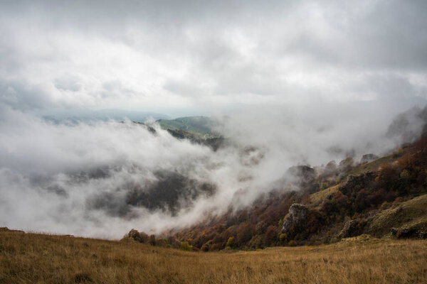 alpine valley with woods variegated from green to yellow to orange with clouds and suggestive fog that envelops the alpine peaks at Durlo in the Lessini park Vicenza