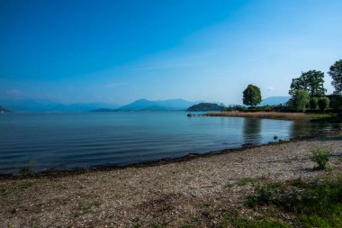 Lombard kıyılarından Maggiore Gölü 'nün panoramik manzarası. Ağaçlar ve Maggiore Gölü' nde balıkçı tekneleri olan büyüleyici küçük limanlar. Varese Lombardy İtalya 'da.