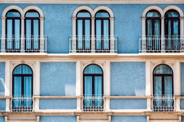 Pencerelerinde mavi duvar ve beyaz balkon perdeleri olan kemerli pencereler. Garda Gölü 'nde, pencereli ve mavi duvarlı Venedik büyük balkonları olan pencereler.