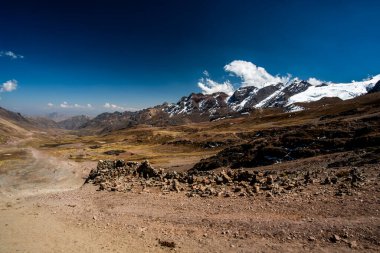 Peru 'nun Cusco bölgesinde, Ausangate yakınlarındaki Peru Andean dağlarında, arka planda platoda mavi gökyüzü ve beyaz bulutlar bulunan tepe ve vadi manzaraları.