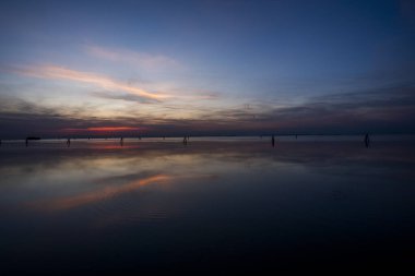 Venedik gölünün sakin sularına kırmızı ve turuncu renklerle yanan günbatımı yansıtılır. Venedik 'teki Venedik Lido' sundan çekilen tuğla ve ağaçlarla.