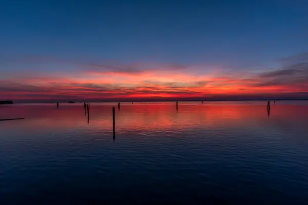 Venedik gölünün sakin sularına kırmızı ve turuncu renklerle yanan günbatımı yansıtılır. Venedik 'teki Venedik Lido' sundan çekilen tuğla ve ağaçlarla.