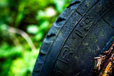 Harap olmuş siyah bir lastiği olan eski bir araba tekerleğinin yakın çekimi ve soyulmuş boyalı paslı bir kenarı.