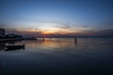 Venedik gölünün sakin sularına kırmızı ve turuncu renklerle yanan günbatımı yansıtılır. Venedik 'teki Venedik Lido' sundan çekilen tuğla ve ağaçlarla.