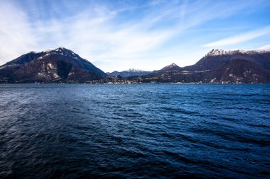 Como Gölü 'nün yüksek dağların arasındaki manzarası sahilde kayaları olan yeşil ağaçlar ve sakin sonbahar suları Alpler ve İtalya' daki Como Gölü 'nün zirveleri arasında muhteşem bir günbatımı.