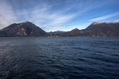 Como Gölü 'nün yüksek dağların arasındaki manzarası sahilde kayaları olan yeşil ağaçlar ve sakin sonbahar suları Alpler ve İtalya' daki Como Gölü 'nün zirveleri arasında muhteşem bir günbatımı.