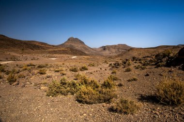 panorama of volcanic mountains and plains and plateaus the peaks and rocks of the south atlas morocco on the atlas between Bab N Ali and Jebel Saghro near Marrakesh and Ouarzazate in Morocco clipart