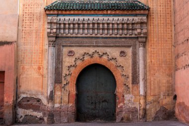 Turuncu duvarda eski yeşil ahşap bir kapı. Fas şehrinin tipik ön cephesinde Fas kemerleri var.